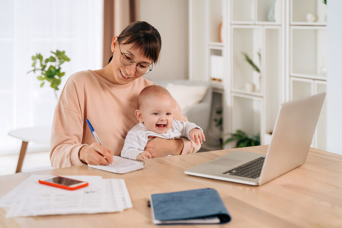 Cheerful Business Mom Holding Her Baby While Working Remotely In